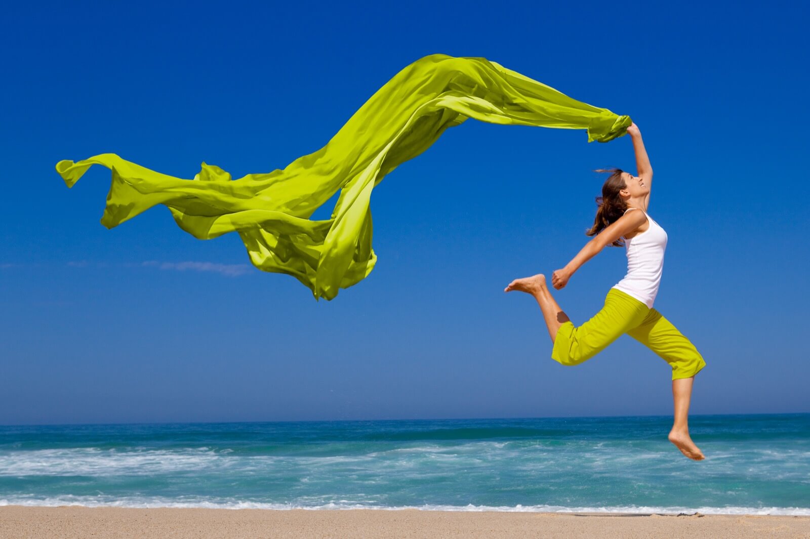 Frau am Strand mit freudigem Luftsprung. Voller Lebensfreude.