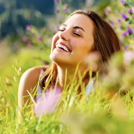 Gesicht einer glücklich lachenden Frau, welche von der Sonne angestrahlt wird.